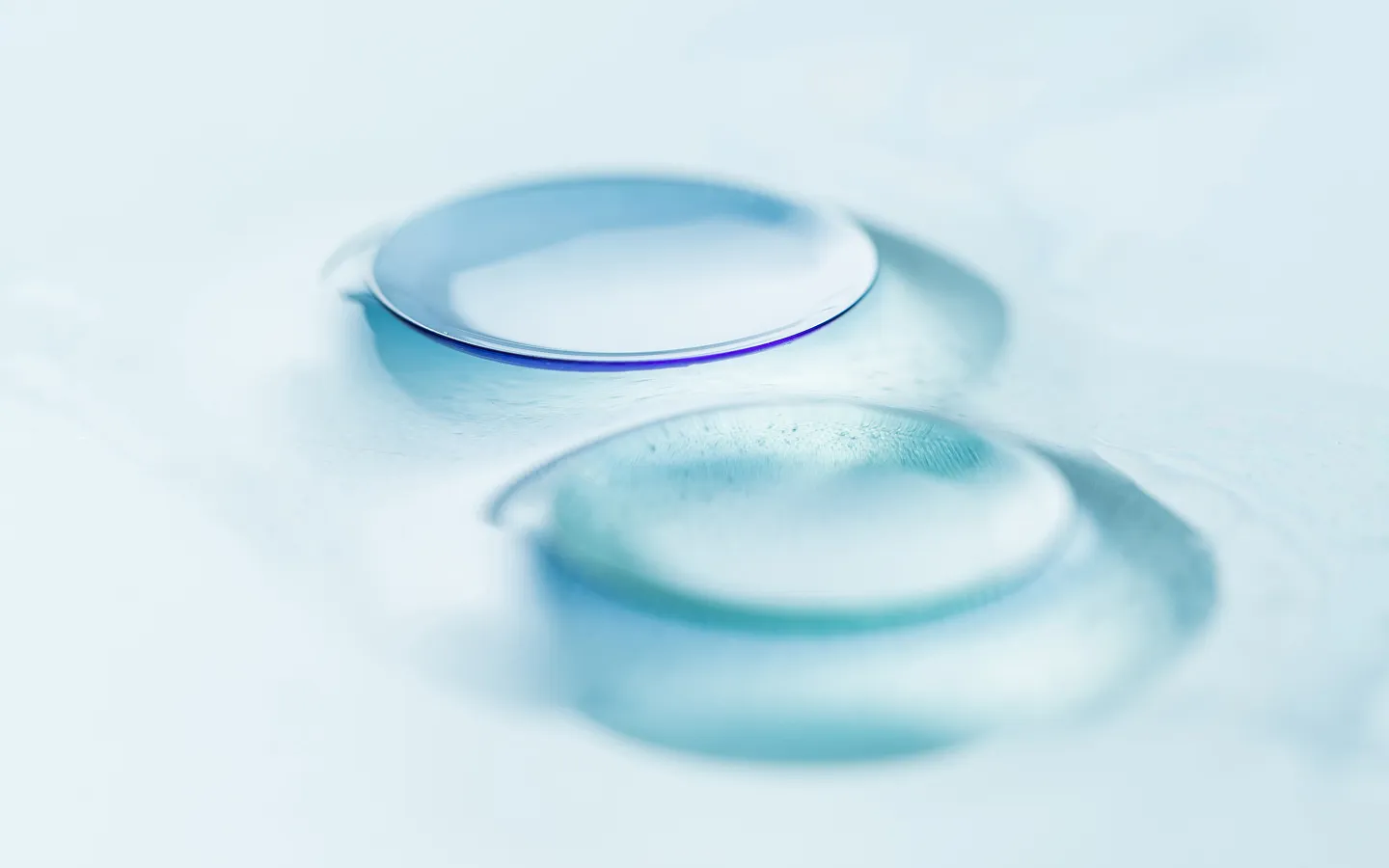Two clear contact lenses resting on a flat surface with a soft blue tint.