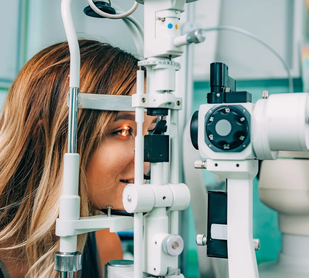Young woman undergoing an eye exam using a slit lamp in an optometrist's office.