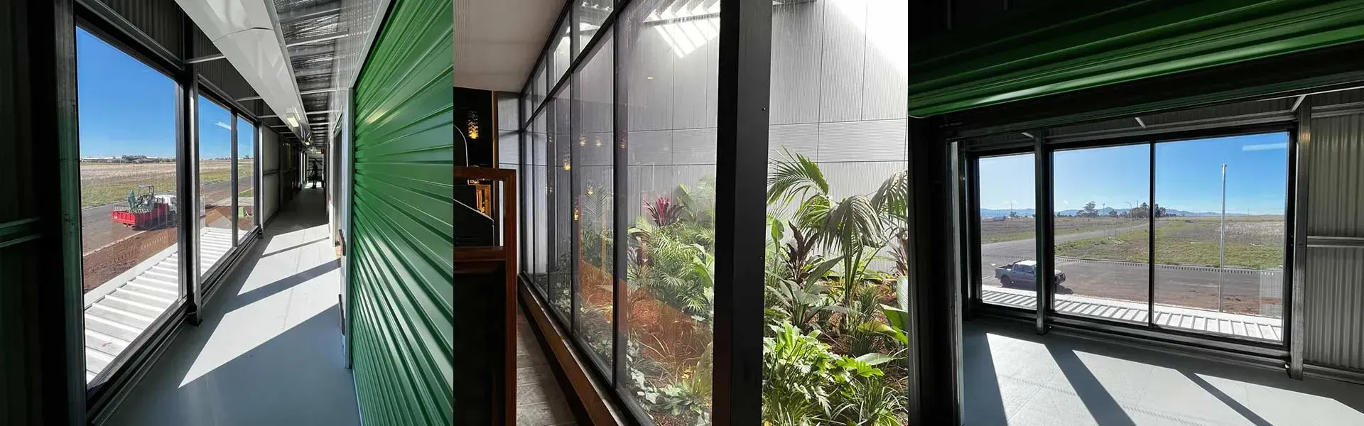 Interior hallway with large windows overlooking an outdoor industrial area and a glass wall revealing an indoor garden with various green plants.