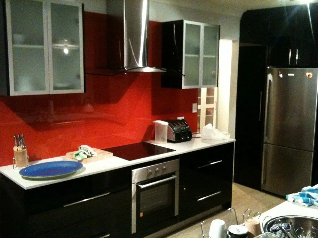 Modern kitchen with black cabinets, white countertop, red glass backsplash, stainless steel stove, oven, and refrigerator.