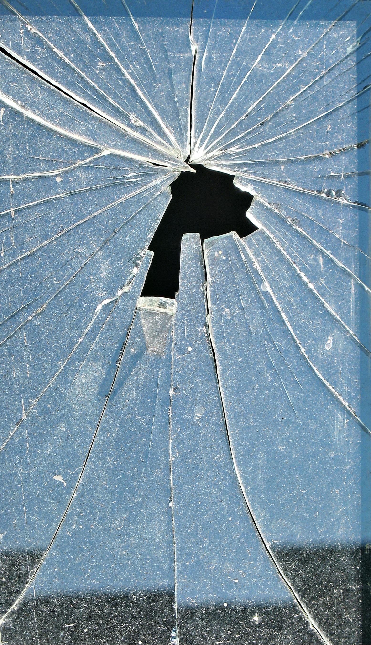 Close-up of a shattered glass pane with a large hole in the center and numerous radiating cracks.