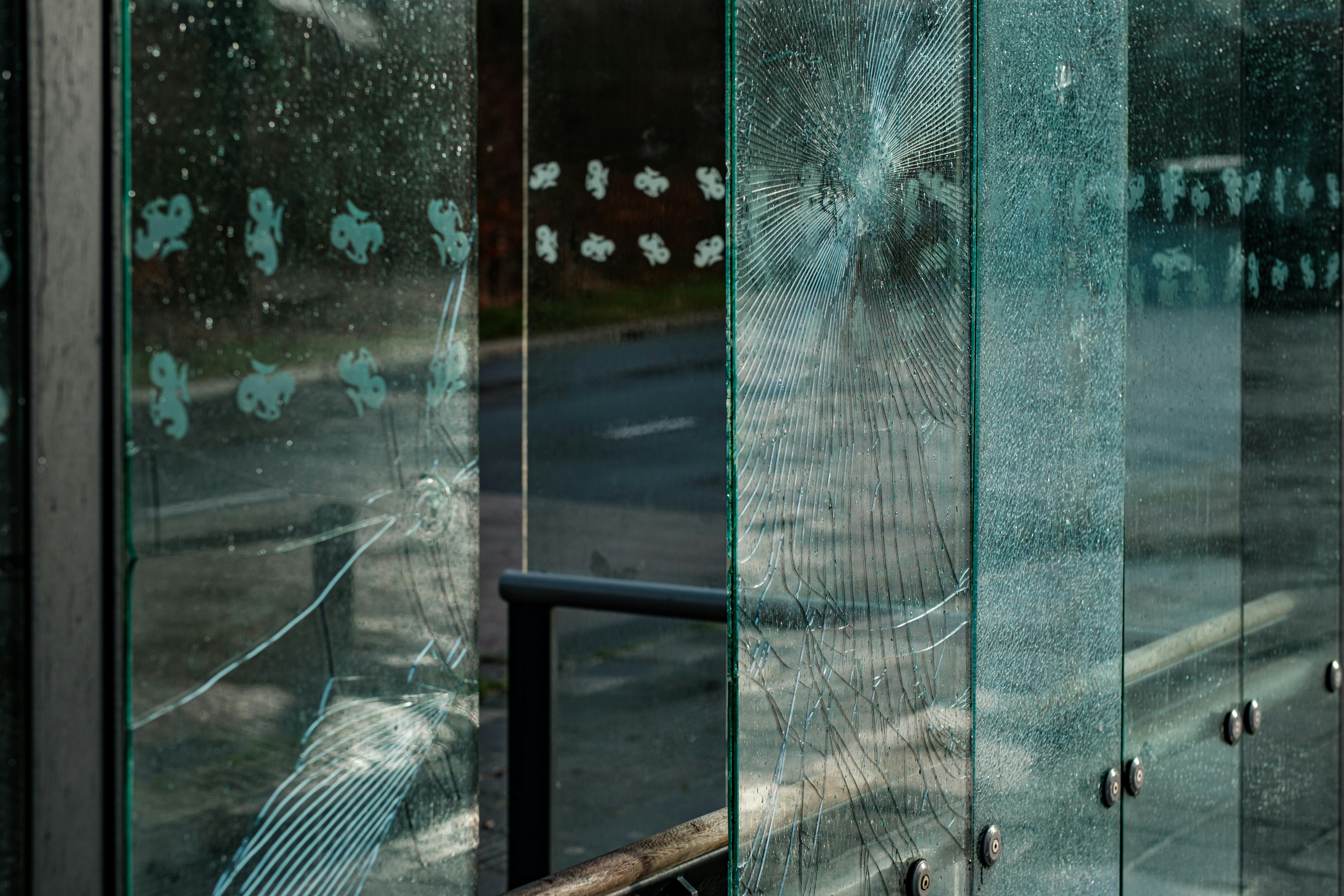 Close-up of shattered and cracked glass panels with circular impact points, part of an outdoor structure.
