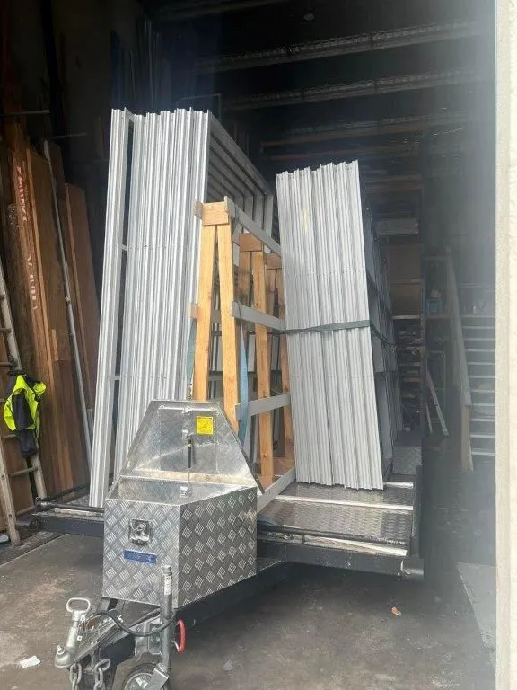 Trailer loaded with stacked metal frames and wooden supports inside a storage area.