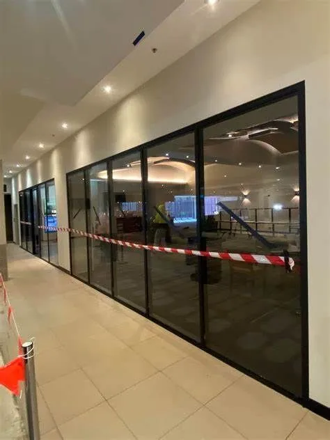 Hallway with large glass windows taped off with red and white caution tape, indicating restricted access.