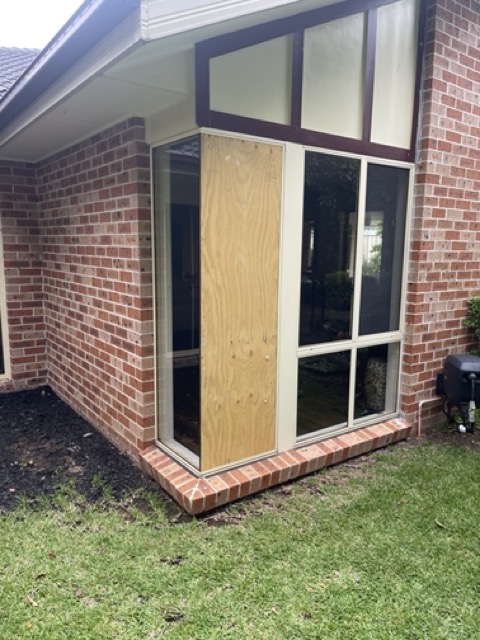 Two workers installing glass panels on a large commercial building with a Panther Glass emergency service truck in the foreground.