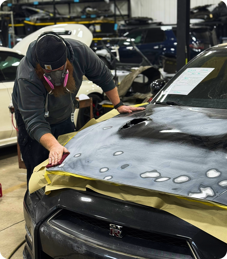 A K-ceps worker is wearing a breathing mask while buffing out a Nissan GTR hood for dents and damage.