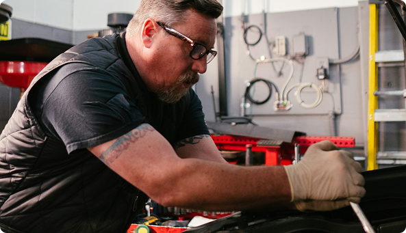 Worker with wrench, working in the engine bay of a car out of the picture.