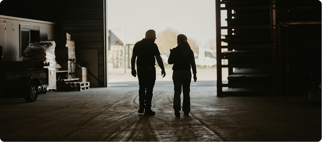 Image of two people in a barn chatting, with the sun at the front, making them dark shadow-like figures.