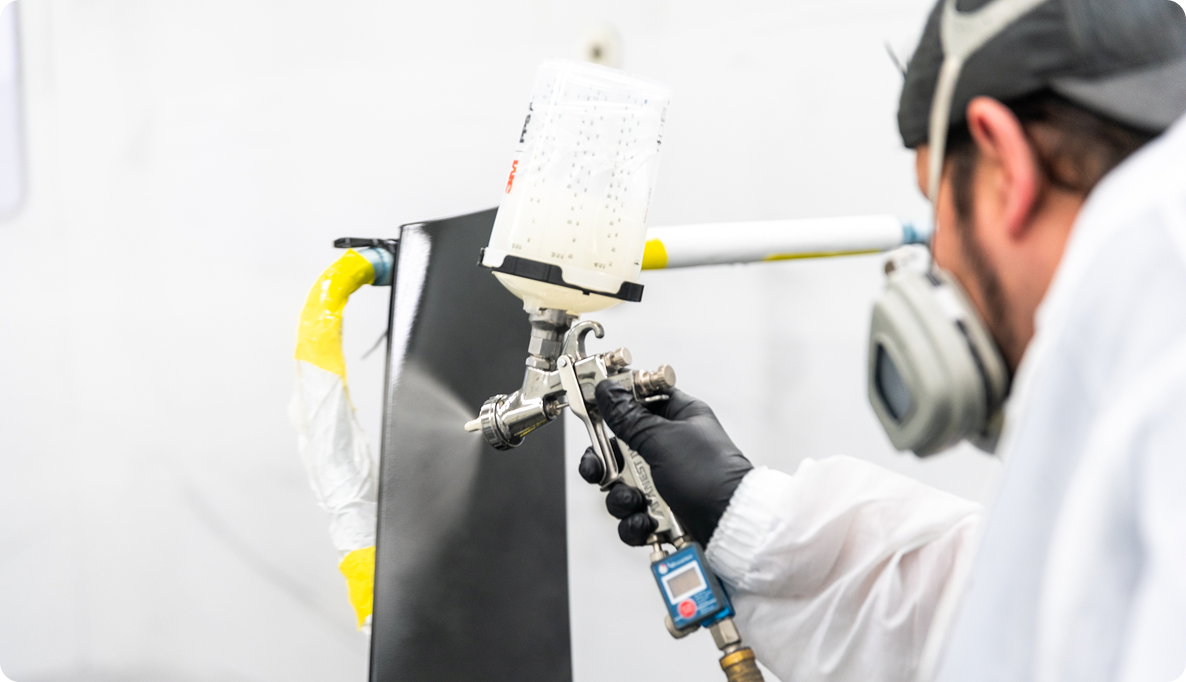 A K-ceps specialized paint worker painting a panel on a car black within the specialty paint booth at the K-ceps Granville location.