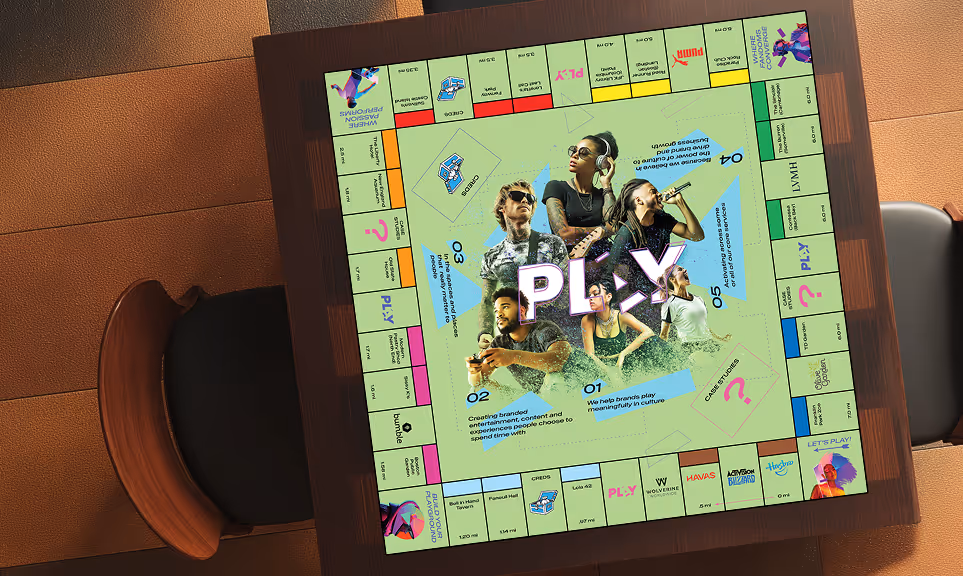 A custom board game on a table featuring a square layout with colorful spaces and images of five diverse people in the center surrounding the text 'PLAY'.