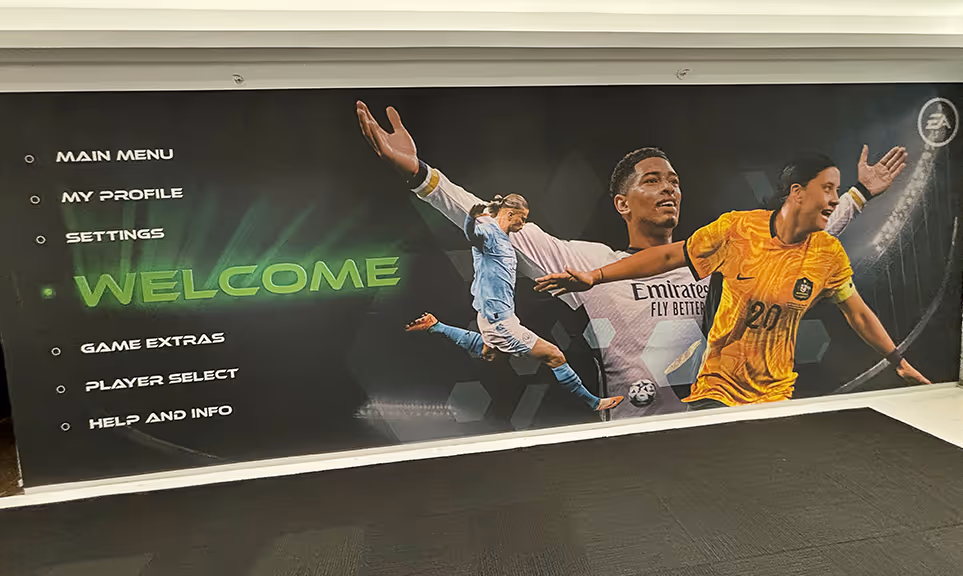 Wall mural with video game menu options and images of three soccer players in action under stadium lights.