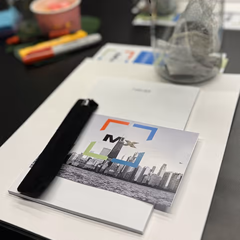 Workspace with a booklet featuring a city skyline and colorful frame, placed on top of papers and a table.