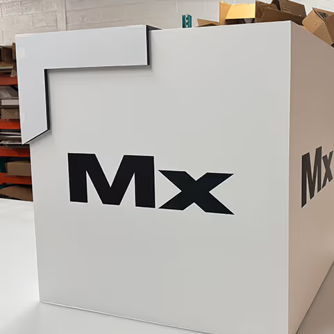 Large white box with bold black letters 'Mx' printed on the front, placed indoors with shelves and cardboard boxes in the background.