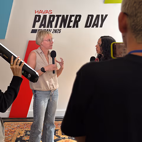 Two women holding microphones and engaging in a discussion during Havas Partner Day April 2025 event, with other people and equipment partially visible.