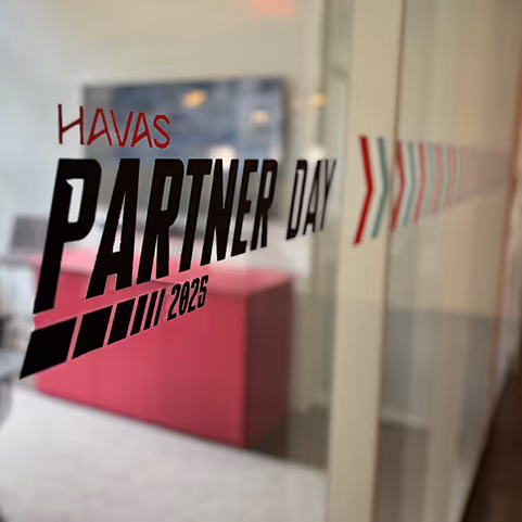Glass panel with 'HAVAS PARTNER DAY 2025' text and arrow graphics inside a modern office space.