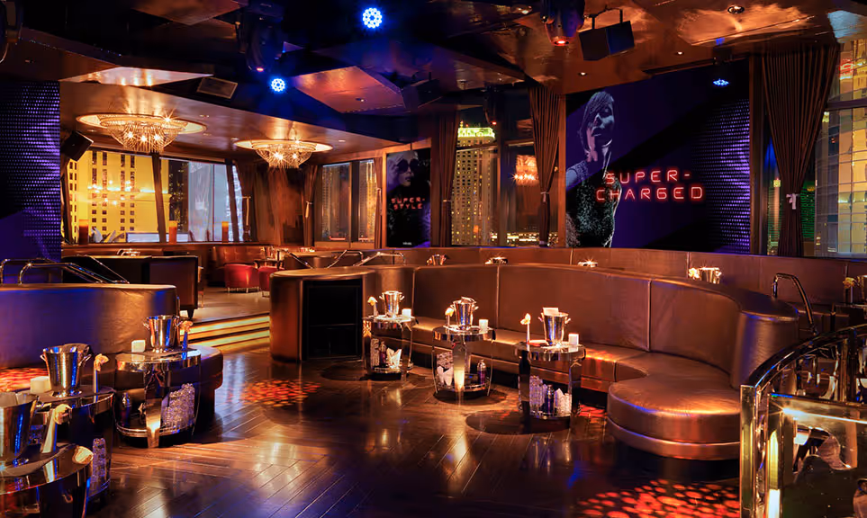 Modern upscale lounge with curved leather seating, small tables with ice buckets, and colorful lighting.