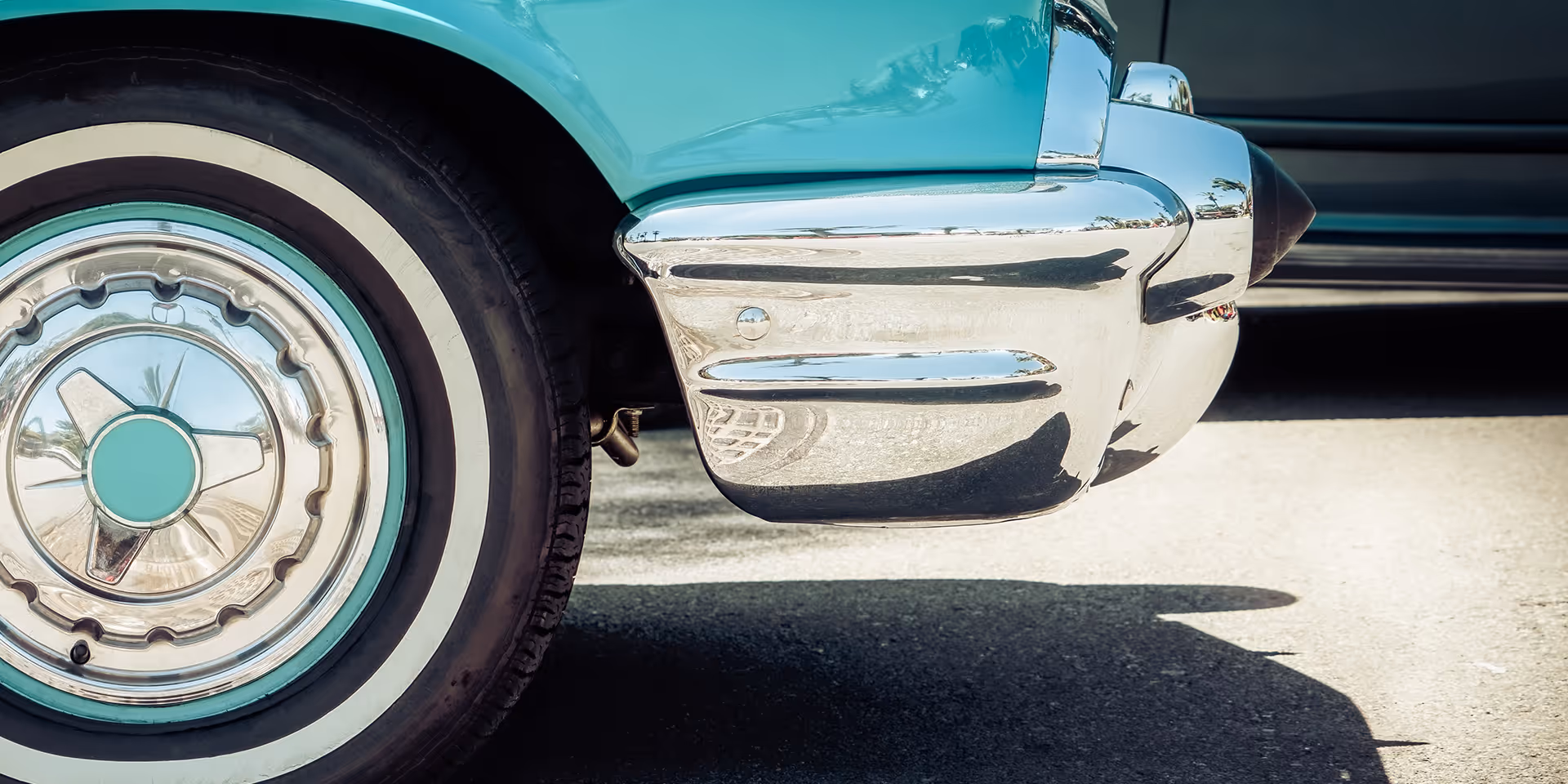 Close-up of the front left wheel and chrome bumper of a vintage turquoise car.