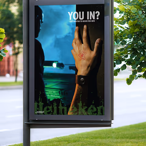 Outdoor advertisement shows a hand with a red star tattoo and wristband, with text 'YOU IN?' and a person holding a flashlight in the background.