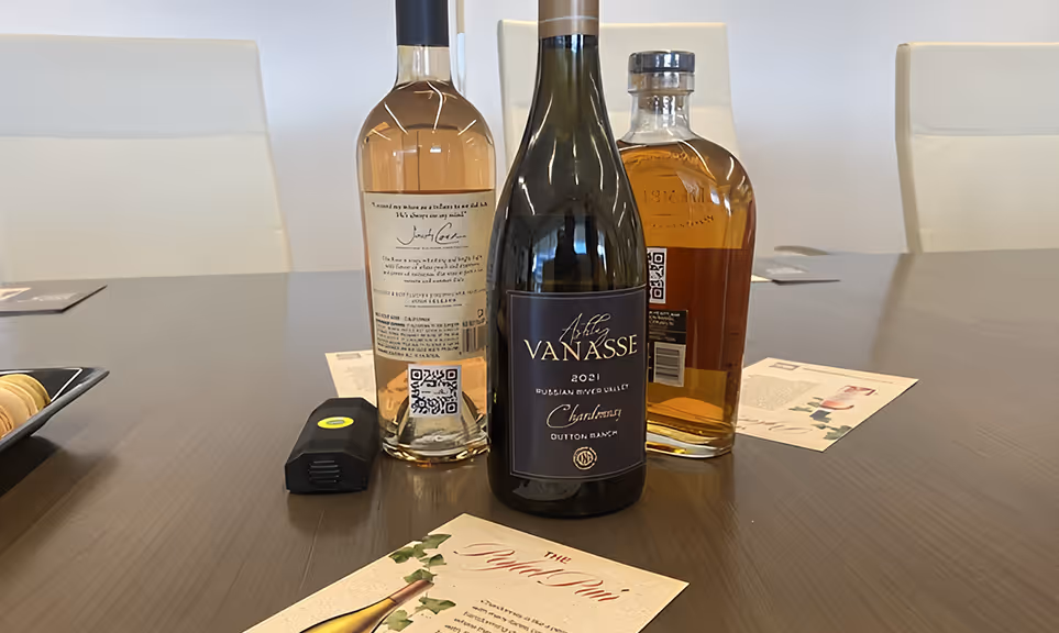 Three bottles of wine and liquor on a dark wood table with white chairs in the background and a menu card in front.