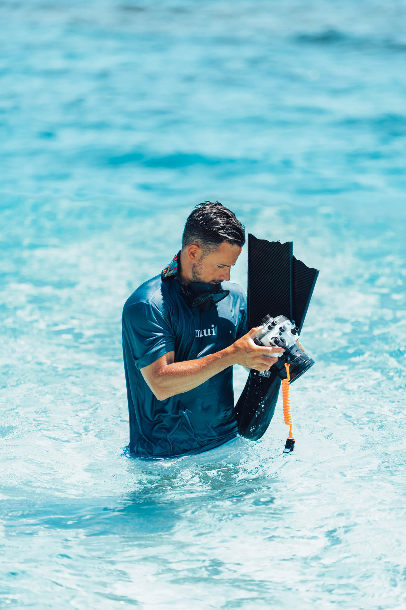 Snorkeler checking an underwater camera with a gold mirrored mask around his neck