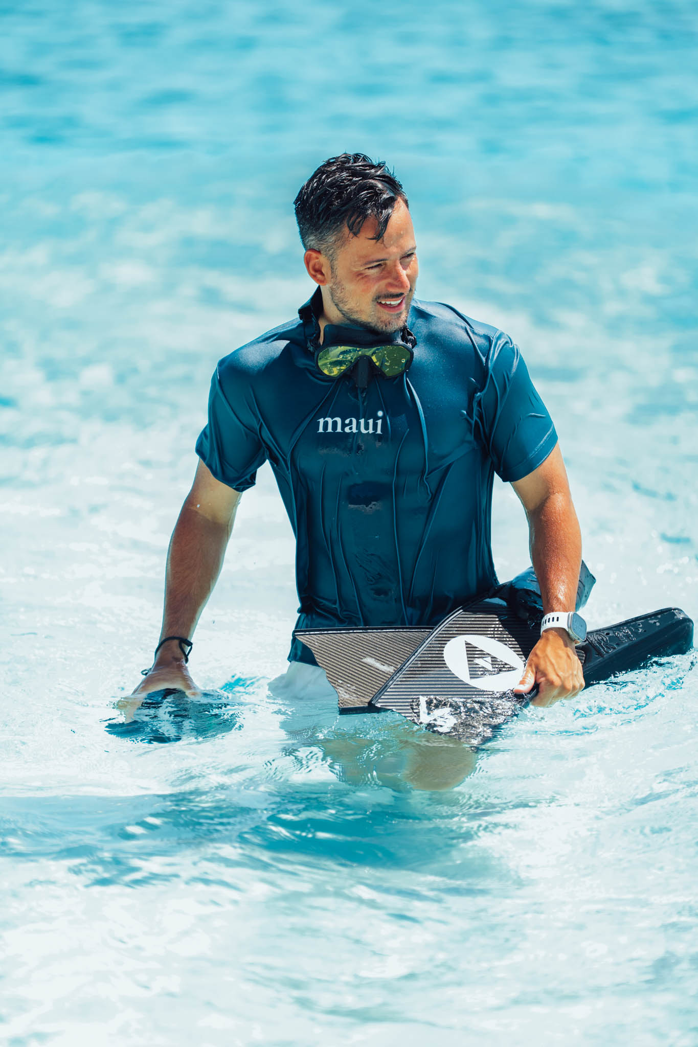 Smiling snorkeler wading out of the water with fins and a mirrored mask