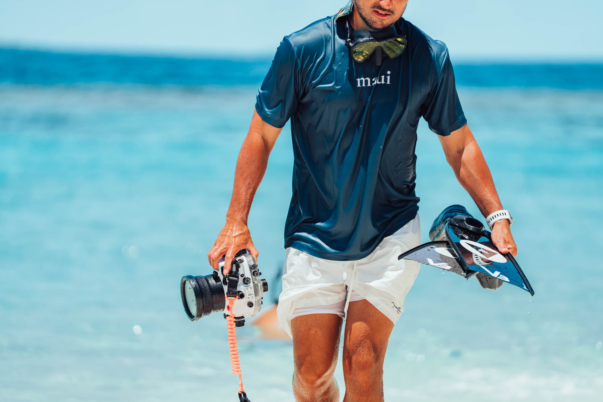 Snorkeler walking out of the sea with a mirrored mask, camera and carbon fins