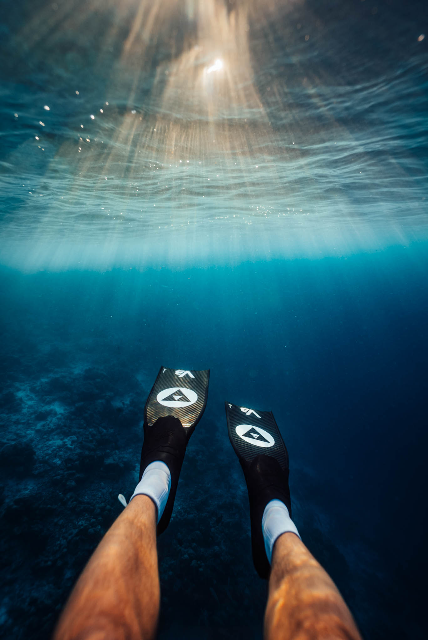 Underwater view of sun rays through the surface above carbon fins