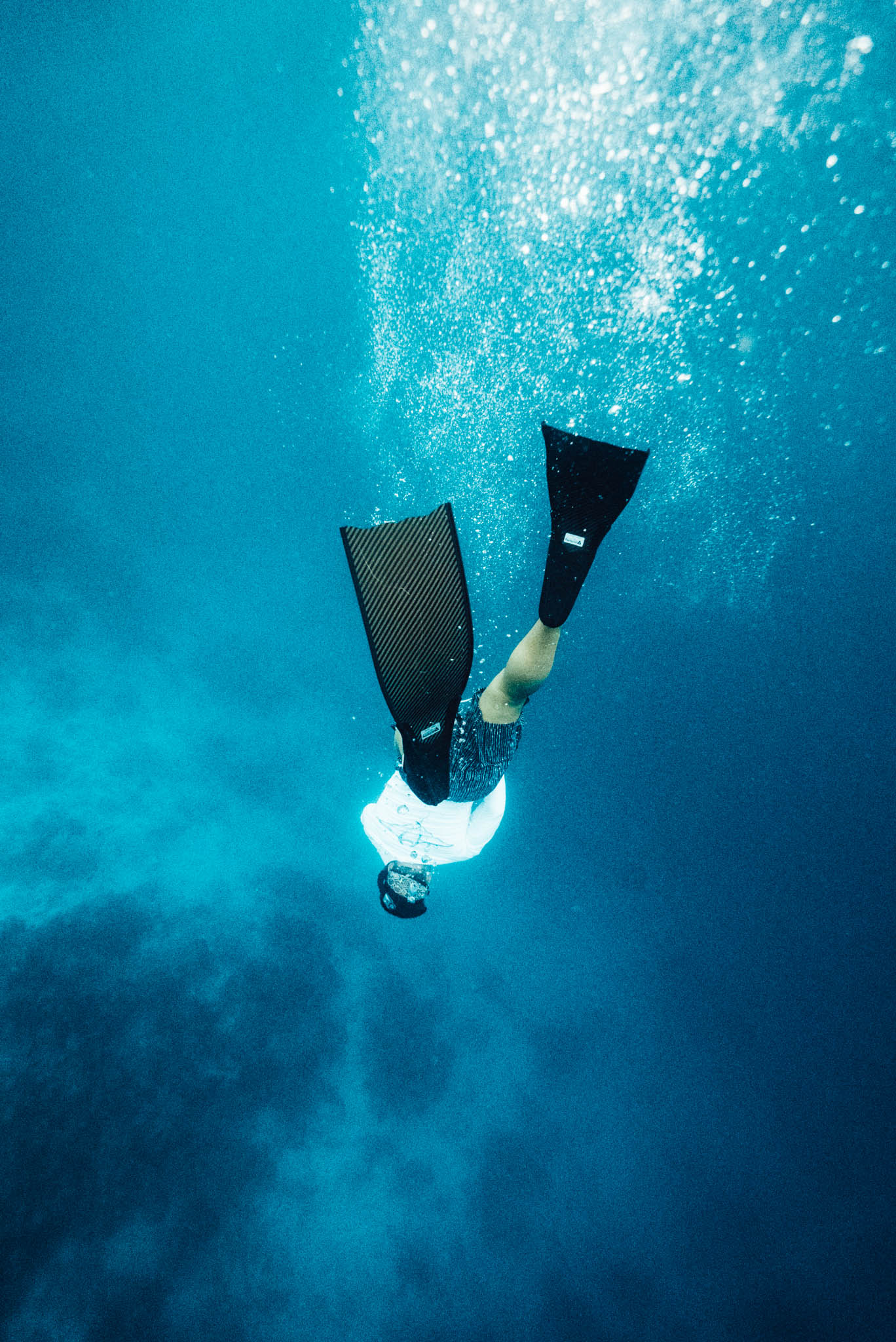 Freediver duck diving into deep blue water with long carbon fins