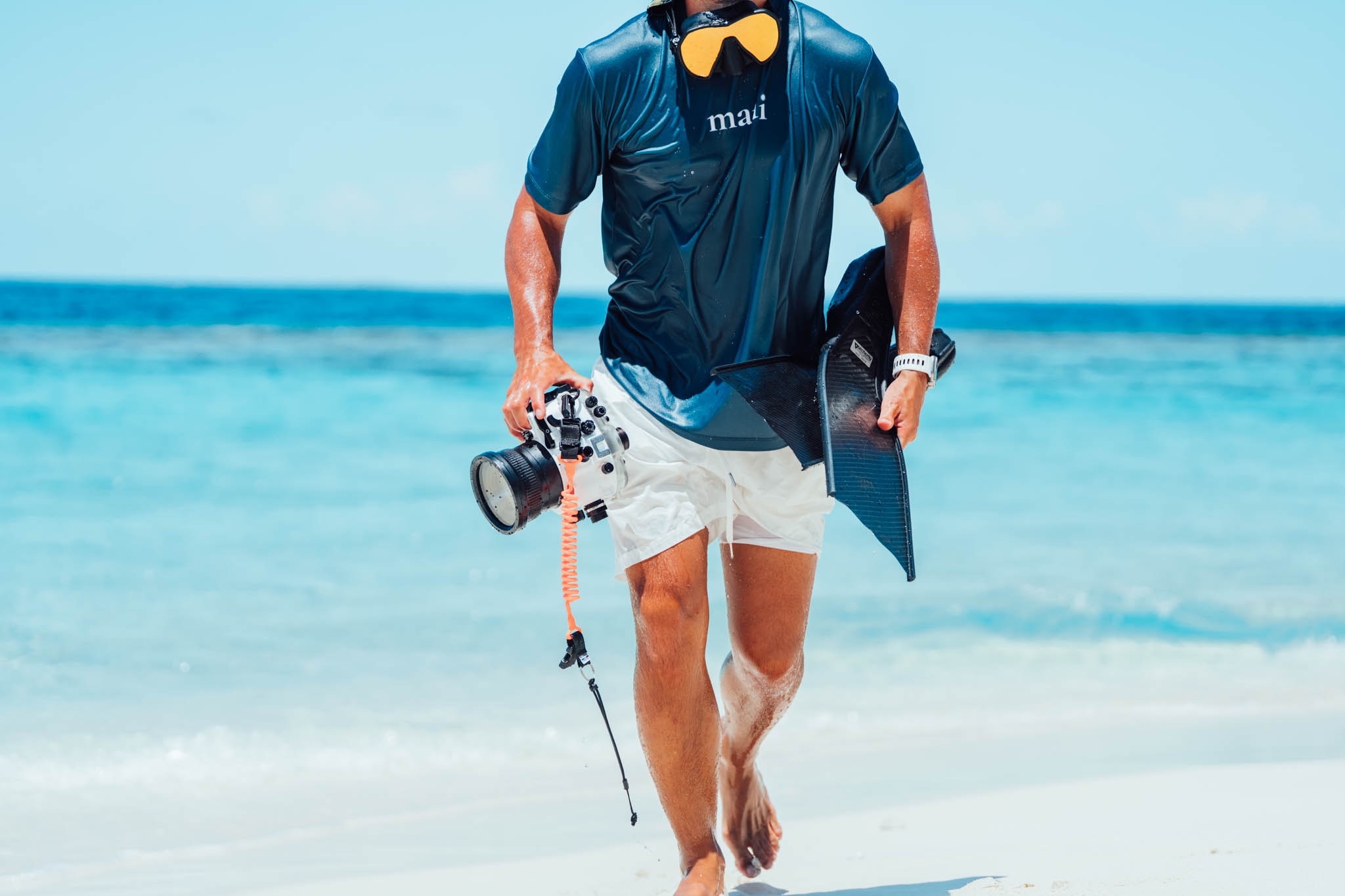 Snorkeler in a Maui shirt walking out of the sea with a SeaFrogs camera housing and carbon fins