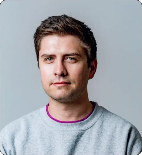 Portrait of a young man with short brown hair wearing a gray sweatshirt against a light gray background.