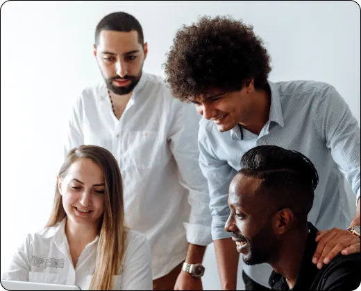 Four coworkers gathered around a laptop, smiling and discussing something on the screen.