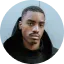 Close-up portrait of a man with short hair and a mustache wearing a black hoodie.