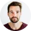 Portrait of a young man with beard and mustache, wearing a white t-shirt against a white background.