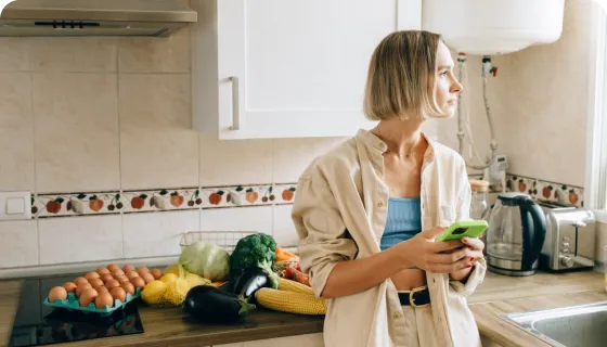 Woman holding green phone in a kitchen with vegetables and eggs on the counter.