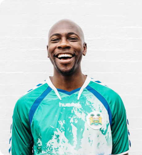 Smiling bald man wearing a green and white Hummel sports jersey with an emblem on the chest.