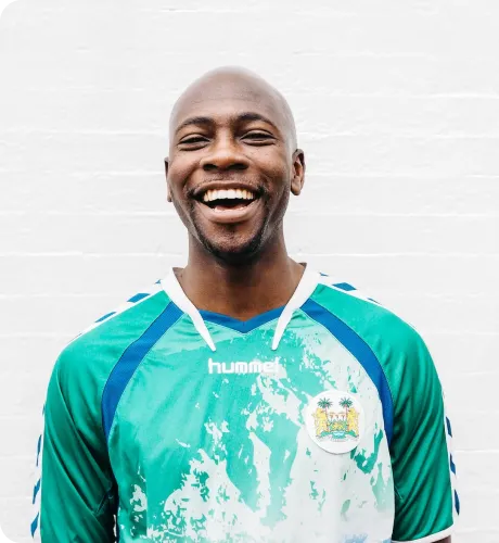 Smiling bald man wearing a green and white Hummel sports jersey with an emblem on the chest.