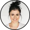 Smiling woman with dark hair in a messy bun wearing a white shirt on a white background.