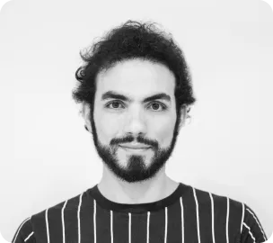 Man with curly hair and beard wearing a striped shirt, smiling slightly against a white background.