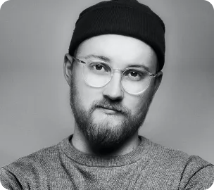 Man with glasses, beard, and black beanie wearing a grey sweater looking at the camera.