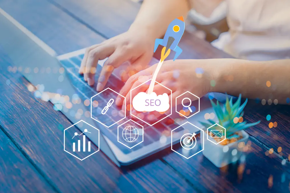 Hands typing on a laptop with SEO-related icons and a rocket symbol.