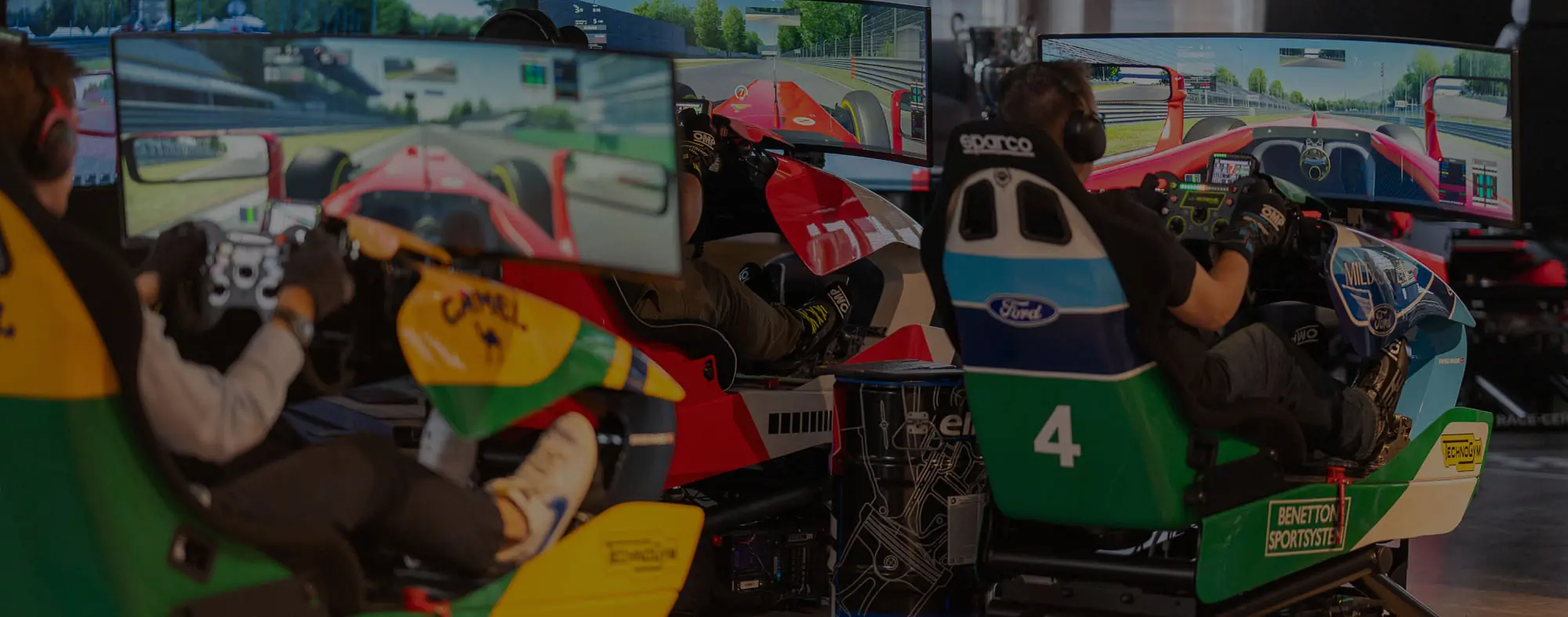 Three people seated in racing simulator cockpits with multi-monitor setups showing a Formula 1 racing game.
