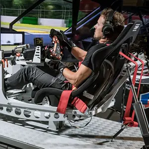 Man wearing headphones and gloves seated in a racing simulator cockpit holding a steering wheel.