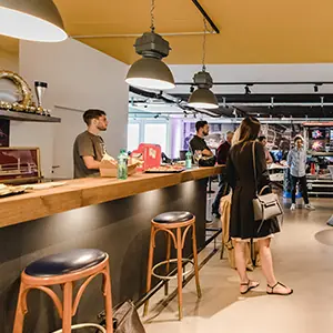 Barista serving customers at a cafe counter with wooden stools and modern hanging lights.