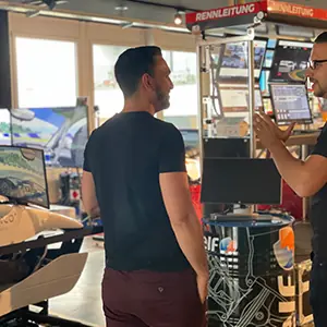 Two men standing and talking in a modern office space with computer monitors and equipment around them.