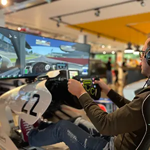 Person wearing headphones using a racing simulator setup with steering wheel and dual monitors displaying a car race.