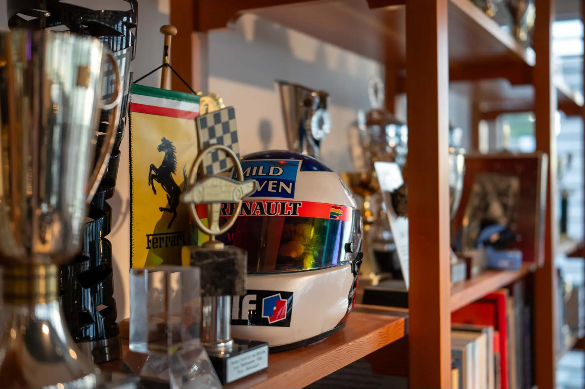 Shelf displaying a racing helmet with Mild Seven and Renault logos, surrounded by trophies and a Ferrari banner.