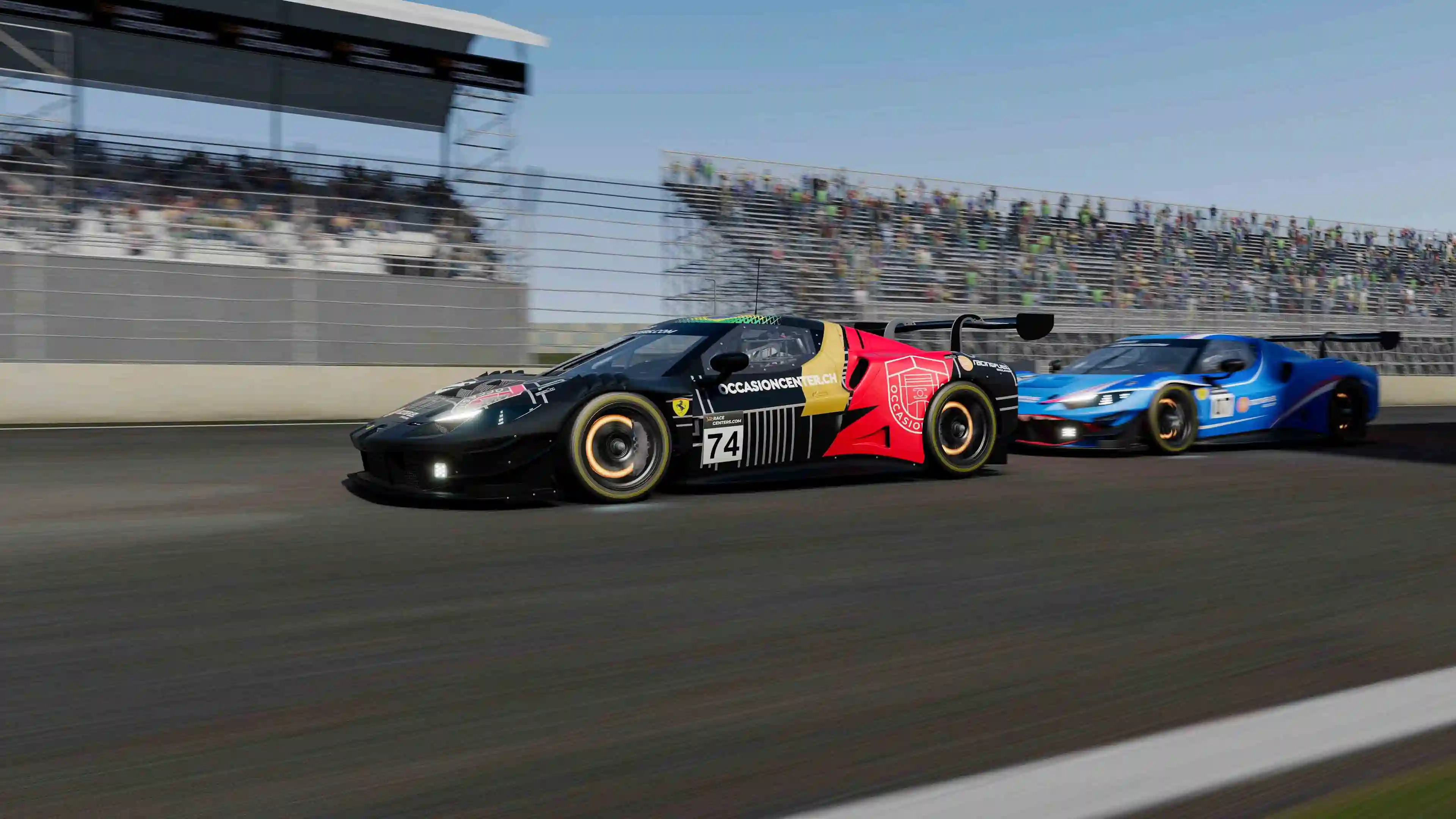 Black and red race car number 74 leading a blue race car on a track with blurred grandstands in the background.