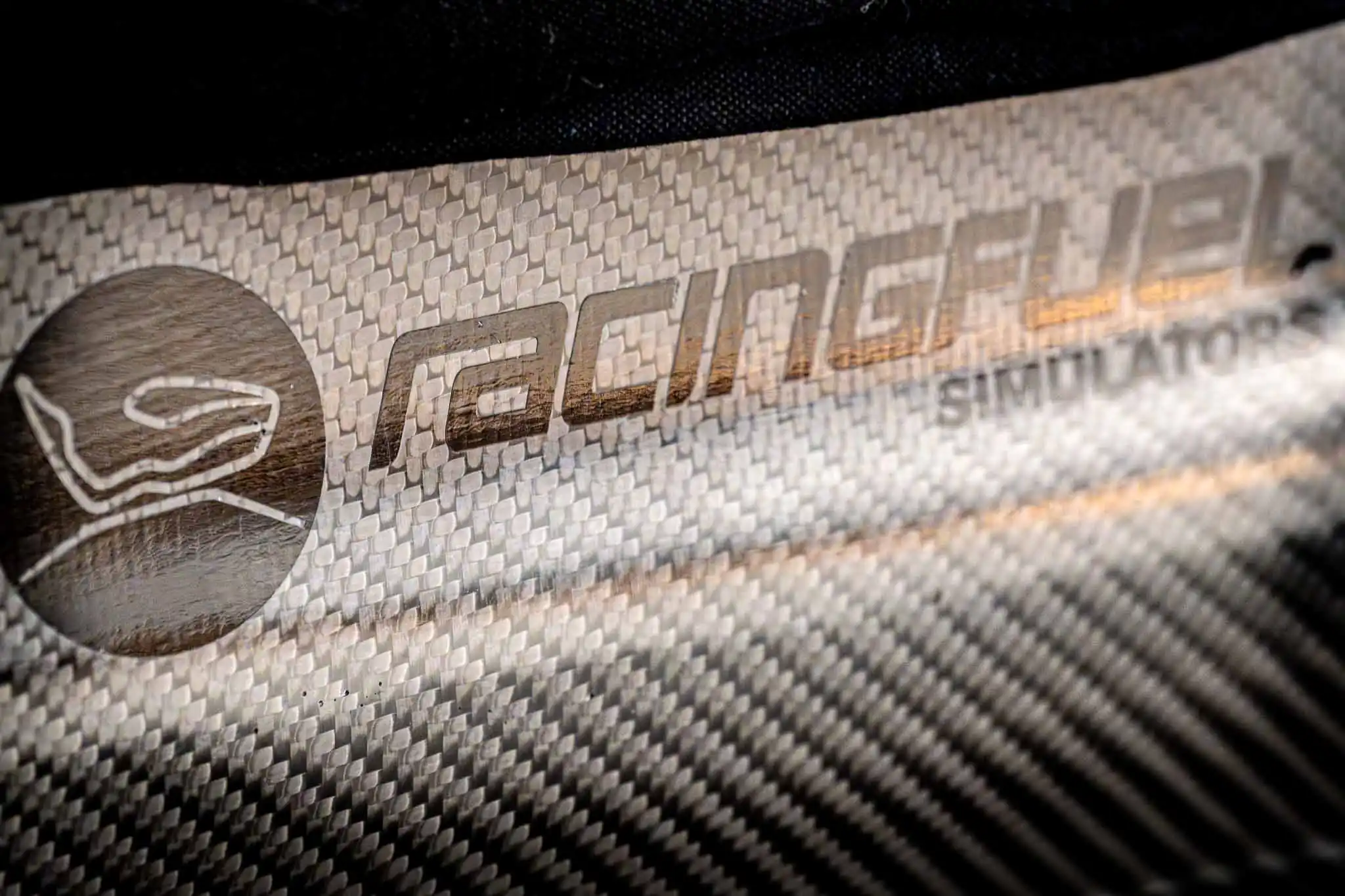 Close-up of a carbon fiber surface with the RacingFuel Simulators logo printed on it.