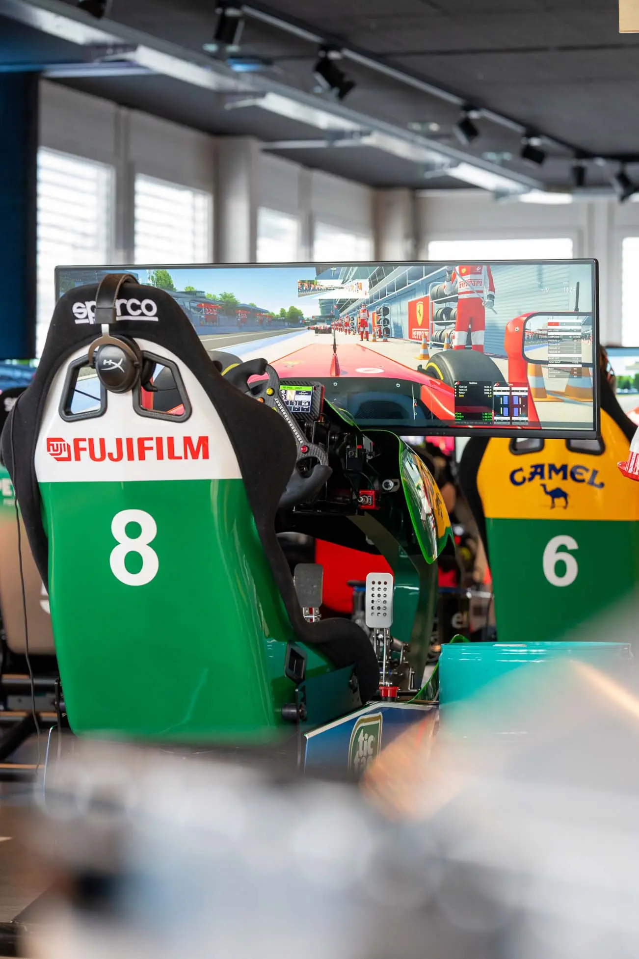 Racing simulator setup with Sparco seat numbered 8 and a large screen displaying a Formula 1 pit lane view.