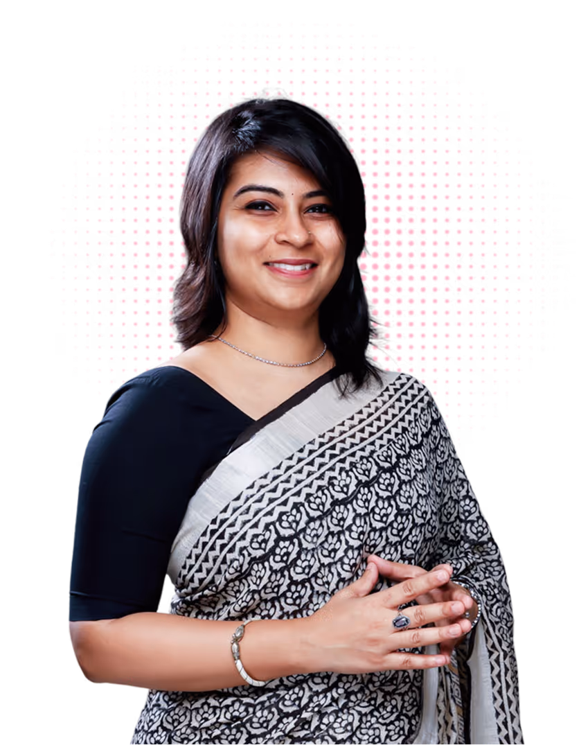 Smiling woman with black hair wearing a black and white patterned saree and jewelry, posed with hands clasped.